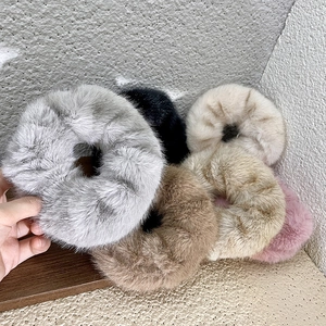 Detail of six plush faux fur hair scrunchies in assorted neutral colors on a wooden surface