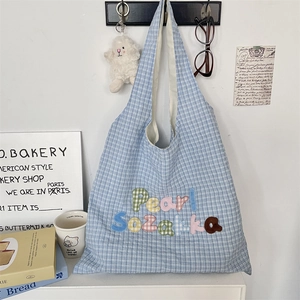 Detail of blue plaid tote bag featuring colorful Pearl Suzakka embroidery in a cozy setting