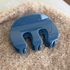 Detail shot of a glossy blue acrylic hair claw clip on soft beige textured fabric