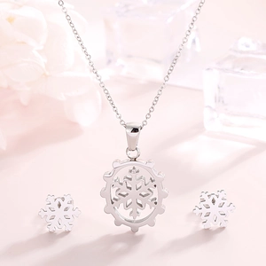 Silver snowflake necklace and earrings set displayed on a soft pink surface