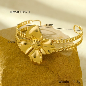 Macro shot of gold floral bangle with Cuban chain band on natural rock base