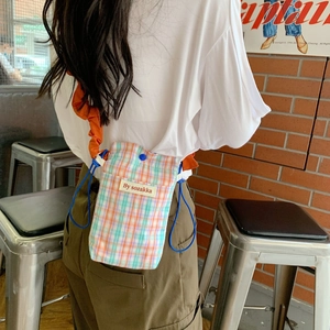 Close-up of a colorful plaid crossbody phone bag with blue drawstring on a model