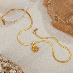 Gold stainless steel necklace with conch shell pendant on a beach sand background