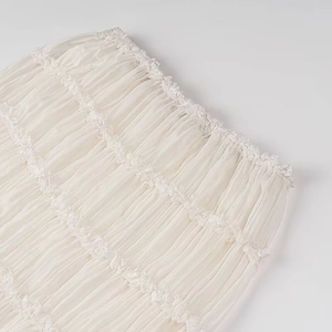 Dettaglio ravvicinato di tessuto in chiffon crema plissettato con bordi in pizzo