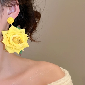 Detailed macro view of yellow fabric rose earrings on a model with green leaf accents