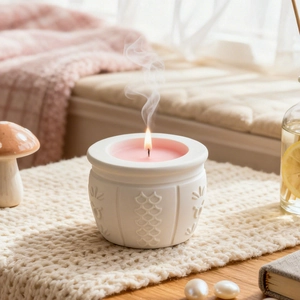 Detailed view of a lit pink candle in a white embossed ceramic jar on a cozy knit surface