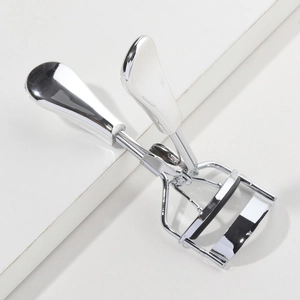 Mini stainless steel eyelash curler with ergonomic handle and black rubber pad on white