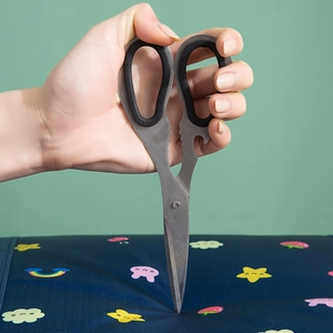Multipurpose kitchen scissors with black rubber handle piercing through blue fabric