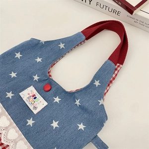 Detail of star-print denim handbag with red ribbon handles and heart lace trim