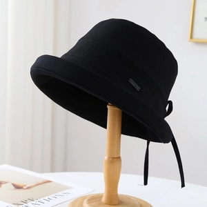 Detail view of black cotton bucket hat featuring a Hand Made metal label and back ribbon tie
