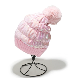 Detail of pink laser surface winter hat with faux fur pompom on a display stand