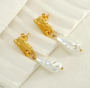 Détail de clous d'oreilles dorés irréguliers avec perles baroques et texture ondulée