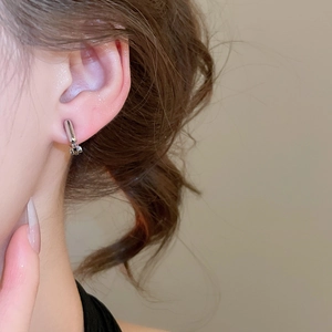 Close-up of silver geometric round ear clip with small pendant worn on ear