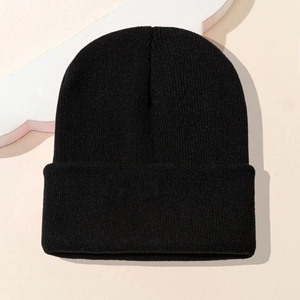 Detailansicht einer schwarzen Strickmütze mit Rippenmuster auf warmem beige Hintergrund