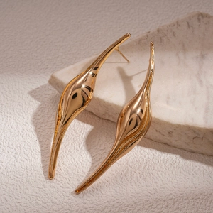 Abstract geometric curved gold earrings displayed on a white marble stone surface