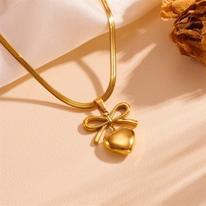 Detail of gold bow and heart pendant necklace on sleek snake chain with elegant styling