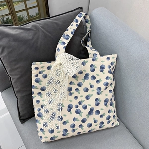 Detail of canvas tote bag featuring blueberry print and delicate white lace bow accent