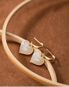 Dettaglio di orecchini a cuore crema su supporto di bambù con finiture dorate