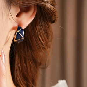 Close-up of model wearing gold vintage C-shape earrings with blue enamel geometric patterns