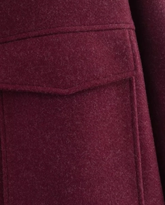 Gros plan du manteau en laine bordeaux montrant la texture, la poche et les coutures