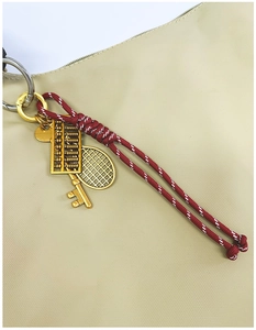 Detail of woven rope keychain with gold abacus, tennis racket and key charms on a bag