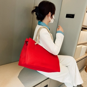 Detail view of large red tote bag with beige rope handles on a model in a modern office