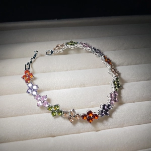 Elegant silver four-leaf clover bracelet with colorful zircons on a beige velvet tray