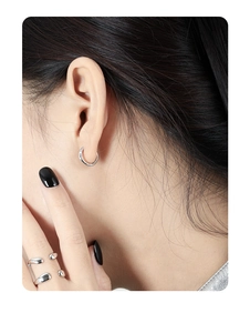 Close-up of minimalist silver hoop earrings and irregular layered ring on a model