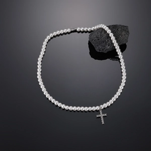 Detailed view of pearl necklace with a silver crystal-set cross on volcanic rock