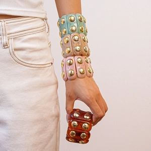 Detail of wide acrylic cuff bracelets with gold stud rivets in multiple fashion colors