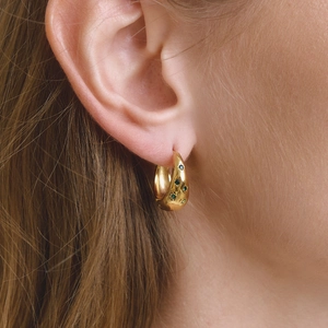 Gros plan de boucles d'oreilles dorées épaisses avec strass verts et noirs portées