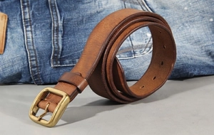 Macro detail of brown leather belt with vintage brass pin buckle on denim fabric