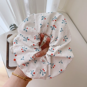 Detailed close-up of a white cotton scrunchie with red cherry prints and dobby texture