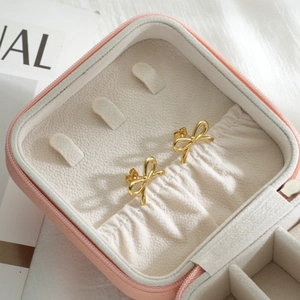 Elegant gold bow earrings displayed on a pink leather jewelry box with a soft warm background
