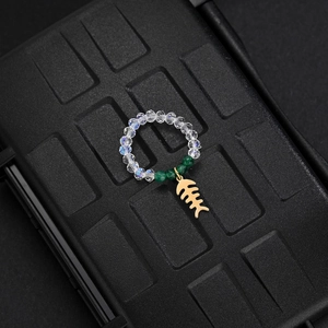 Macro detail of elastic bead ring featuring clear green beads and gold fishbone charm