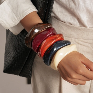 Gros plan de bracelets épais en acrylique ondulés en ambre, bordeaux et ivoire sur poignet