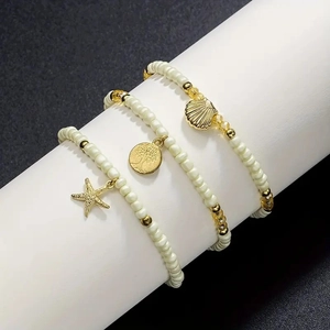 Detailed view of three cream bead bracelets with gold starfish, tree of life, and shell charms