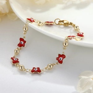 Elegantes vergoldetes Evil Eye Armband mit rotem Emaille-Schmetterling auf weißem Keramiktablett