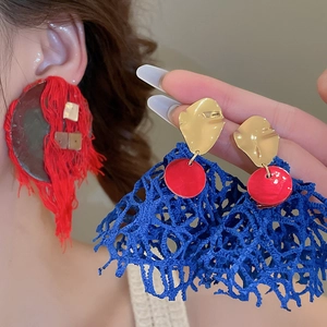 Macro detail of red fringe tassel earrings and blue woven sphere dangles for women