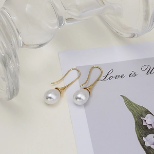 Elegant gold drop earrings with white water-drop pearls displayed on artistic background
