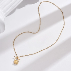 Detailed view of a gold lock pendant necklace with bead chain on white background