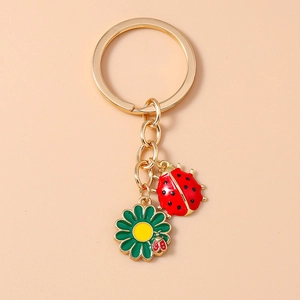 Detail of a golden keychain with red ladybug and green floral enamel charms on a chain