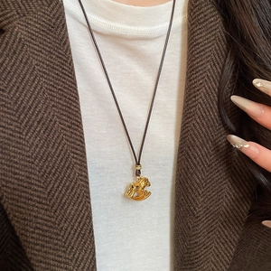 Detailed close-up of a gold rocking horse pendant on a brown cord worn by a model