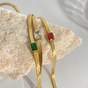 Golden snake chain necklaces with green, white, and red zircon stones on stone background