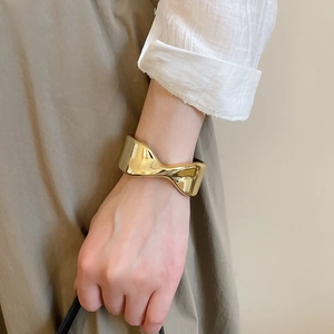 Detail shot of a wide gold cuff bracelet featuring a sculptural, flowing fluid design