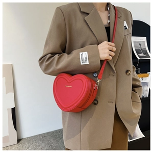 Dettaglio della borsa a tracolla rossa a forma di cuore con scritte dorate su blazer
