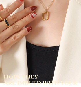 Detail of gold geometric hollow rectangle pendant necklace and black enamel ring