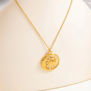 Detailed close-up of 18k gold celestial sun and moon pendant on a minimalist necklace