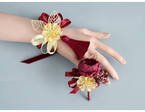 Close-up of wine red silk wrist corsage and matching boutonniere with gold leaves