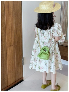 Detail of green drawstring bucket bag with gold chain and pearl strap on floral dress